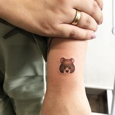 a person with a small bear tattoo on their left wrist and the other hand behind her arm