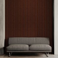 a gray couch sitting in front of a wooden wall with vertical slats on it