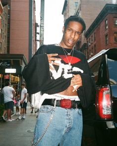 a young man standing in front of a car on the street wearing a sweater and jeans