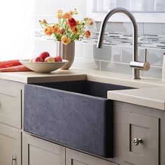 a kitchen sink sitting under a faucet next to a bowl of fruit and flowers