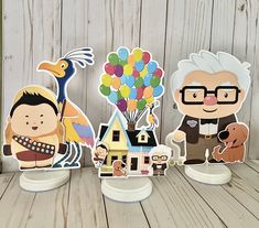 three paper cutouts of people and animals with balloons in the air on a wooden table