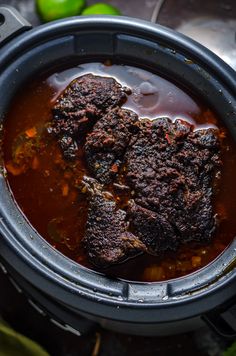 a pot filled with meat and sauce on top of a table next to limes