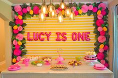 a table topped with lots of food next to a yellow and pink wall covered in balloons