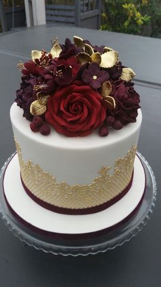 a white and gold cake with red flowers on top