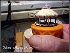 a miniature carousel is being held up by someone's hand in front of an oven