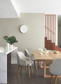 a dining room table with chairs around it and a clock on the wall behind it