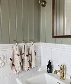 two towels hanging on the wall above a sink in a room with green walls and white tiles