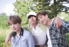 three boys are posing for the camera in front of some trees and grass with their arms around each other