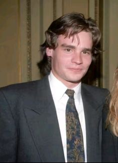 a man in a suit and tie standing next to a blonde haired woman with long hair