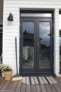 a black double door on the side of a white house with a broom and potted plant next to it