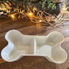 two white dishes sitting on top of a wooden table next to some plants and lights