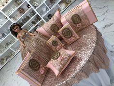 a barbie doll sitting on top of pillows in front of a table with pink and gold decorations