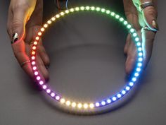 two hands holding a circular light up ring with colored lights on each side and the other hand touching it