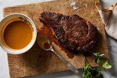 a steak on a cutting board next to a bowl of soup