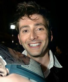 a smiling man holding an open book in his right hand