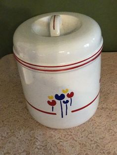 a white ceramic container with flowers painted on the front and sides, sitting on a table