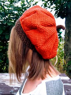 a woman wearing an orange knitted hat on top of a wooden bench next to trees