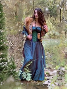 a woman in a blue dress and fur stoler is walking through the woods with trees