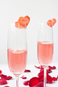 two wine glasses filled with pink liquid and garnished with rose petals on a white surface