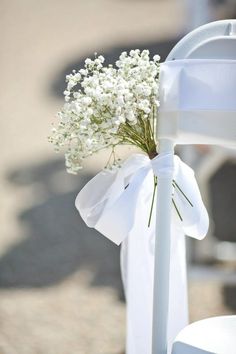 a bouquet of white flowers is tied to the back of a chair at a wedding