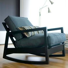 a black rocking chair in front of a window with a striped pillow on the seat