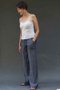 a woman standing in front of a gray background wearing blue jeans and a white tank top