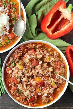 two bowls of chili and rice on a wooden table with green beans, red peppers, and tomatoes