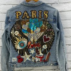 a jean jacket with sequins and patches on it hanging from a brick wall