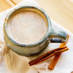 a cup of coffee with cinnamon sticks next to it on top of a white napkin