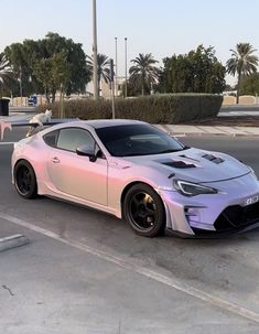 a pink and silver sports car parked in a parking lot with palm trees behind it