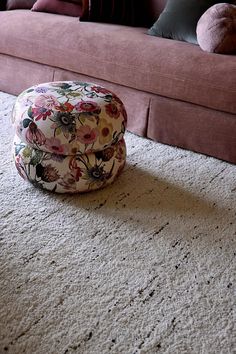 a flowered hat sits on the floor in front of a pink couch with pillows