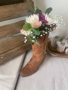 a cowboy boot with flowers in it sitting on a bed next to a wooden box