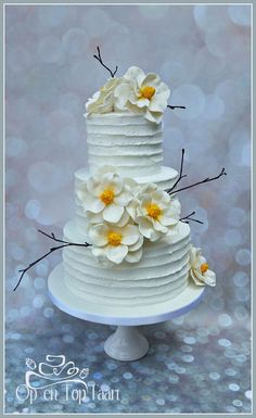 a three tiered cake with white flowers on the top and yellow petals on the bottom