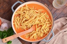 a pot filled with pasta and sauce on top of a wooden table next to an egg