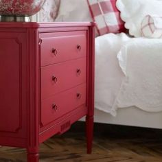 a red chest of drawers sitting on top of a wooden floor next to a bed