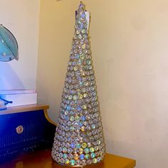 a small christmas tree made out of glass beads on a table next to a lamp