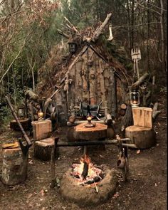 an outdoor fire pit in the middle of a forest with lots of logs and chairs around it