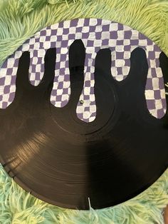 a black record with purple and white checkered design on the side sitting on green carpet