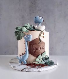 a cake decorated with dinosaurs and leaves on top of a white table next to a gray wall