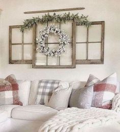 a living room with white couches, pillows and wreaths hanging on the wall