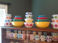 a display case filled with lots of colorful bowls on top of wooden shelves next to a window