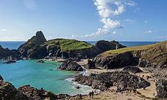 people are walking on the beach next to some rocks and blue water with green hills in the background