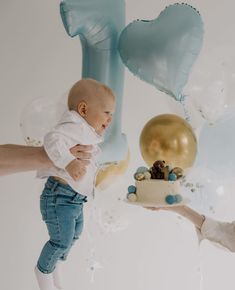 a woman holding a baby in front of balloons and a cake with the number one on it