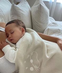 a woman holding a baby wrapped in a blanket while laying on top of a bed