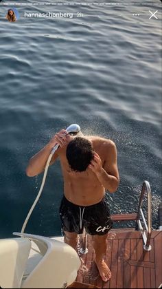 a man standing on top of a boat next to the ocean with his headphones up