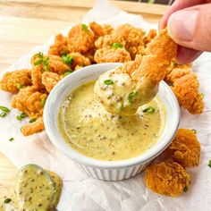 a person dipping some kind of food into a small white bowl with tater tots in it