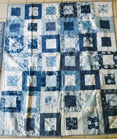 a blue and white quilt is laying on top of a tile floor next to a wall