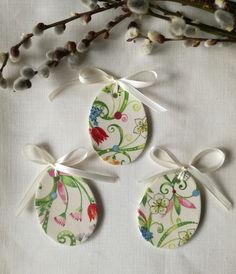 three ceramic ornaments with ribbons tied around them on a white tablecloth next to flowers