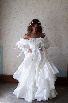 a woman in a white dress is standing against a wall with her hands on her hips