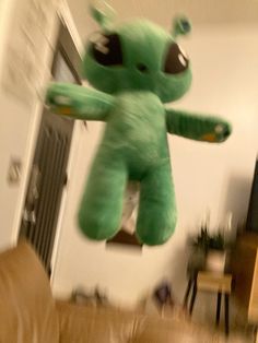 a green stuffed animal flying in the air over a living room with a couch and chair